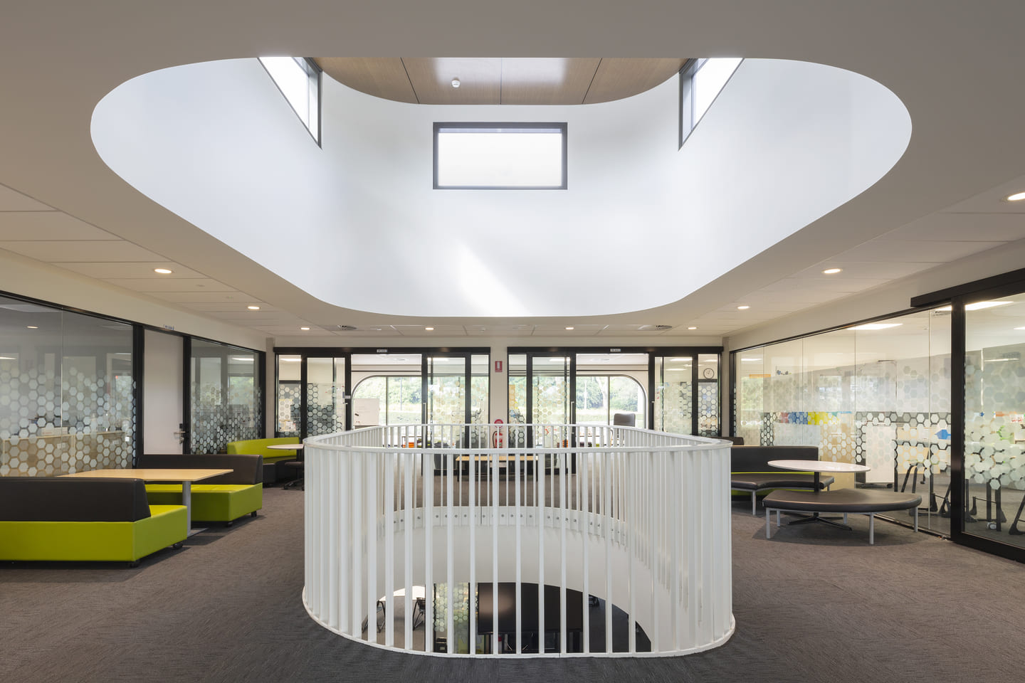 Rows of desks in an office space, with an acoustic ceiling and glazed partitions.